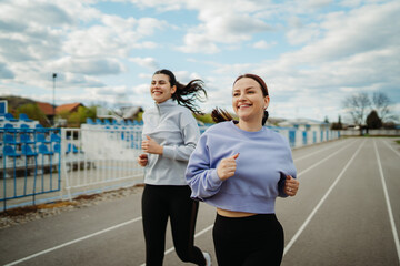 Two female friends running or jogging on stadium doing sport activities