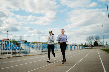 Two female friends running or jogging on stadium doing sport activities