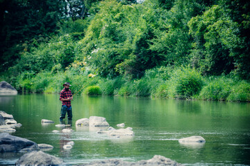 Fisherman fishing on a rever. Relaxed fisher man with a fishing rod on a summer day.