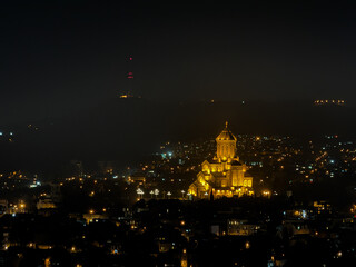 Obraz premium Sameba Cathedral illuminated at night in Tbilisi, Georgia, with glowing city lights and distant TV tower