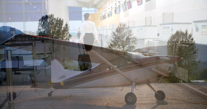 Showing woman in business attire walking through airport check-in with propeller plane and suitcase