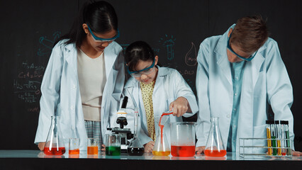 Smart girl pour colored solution in to beaker while diverse student excited about doing experiment....