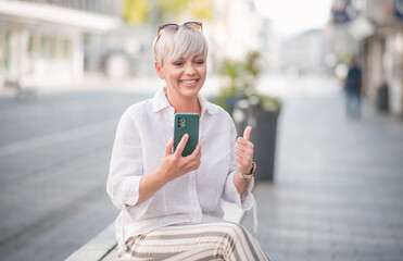 Happy trendy adult woman with smartphone and gesturing like. Pleased woman using the phone....