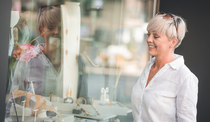Happy woman looking at showcase or shop window chooses jewelry in store. Shopping time. Outdoors - outside