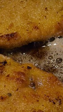 Two golden-brown breaded pork cutlets (schabowe) are frying in bubbling hot oil in a dark pan. The crispy coating and the sizzling oil are clearly visible in this close-up shot. video 4k