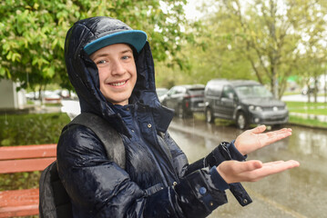 Portrait of a 12 year old boy wet in the rain. Schoolboy in a hooded jacket and with a backpack,...