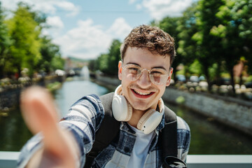 Young adult man student smiling while taking self portrait with smartphone