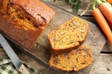 Homemade carrot cake with nuts, knife and vegetables on wooden table, flat lay