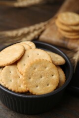 Tasty salty crackers and wheat spikes on wooden table, closeup