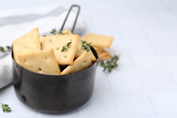 Tasty salty crackers and thyme on white tiled table, closeup. Space for text