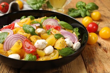 Tasty salad with yellow tomatoes, basil, onion and mozzarella cheese on wooden table, closeup
