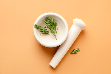 Ceramic mortar with rosemary and pestle on light brown background, top view