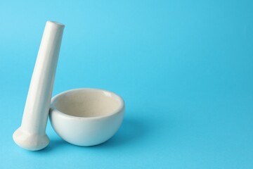Ceramic mortar and pestle on light blue background, closeup. Space for text