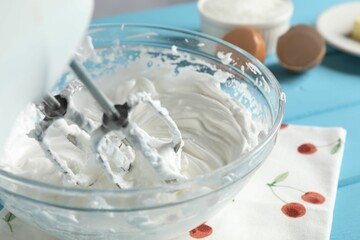 Whisking cream with hand mixer at light blue table, closeup