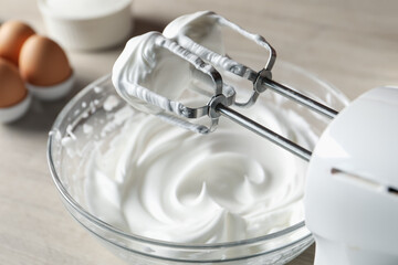 Hand mixer with whisks and whipped cream on table, closeup