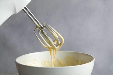 Hand mixer with whisks and bowl of dough on grey background, closeup