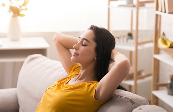 Keep calm and stay home. Peaceful young woman relaxing on sofa in living room - Powered by Adobe