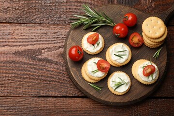 Tasty crackers with cream cheese, rosemary and tomatoes on wooden table, top view. Space for text