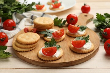 Tasty crackers with cream cheese, tomatoes and parsley on white wooden table, closeup