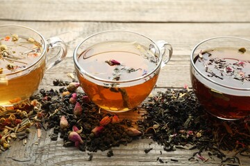 Different herbal teas and dry leaves on wooden table, closeup