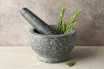 Stone mortar with rosemary and pestle on light table, closeup