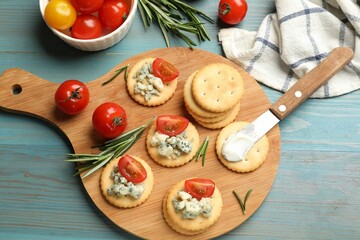 Tasty crackers with blue cheese, rosemary and tomatoes on wooden table, flat lay