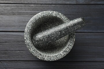 Stone mortar and pestle on black wooden table, top view