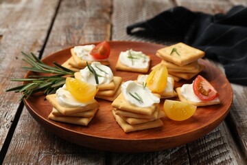 Tasty crackers with cream cheese, rosemary and tomatoes on wooden table, closeup