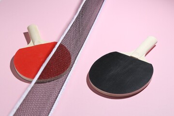Ping pong rackets and net on pink background, closeup