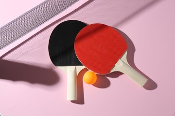 Ping pong rackets, ball and net on pink background, flat lay
