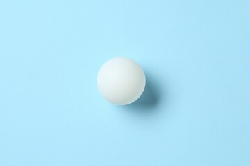 Ping pong ball on light blue background, top view