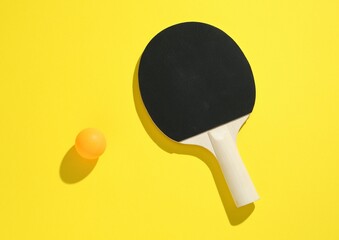 Ping pong racket and ball on yellow background, top view