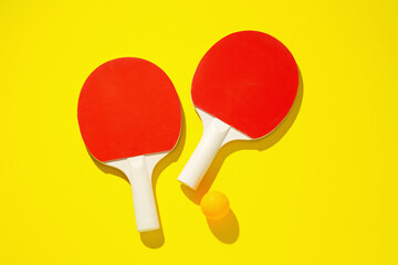 Ping pong rackets and ball on yellow background, top view
