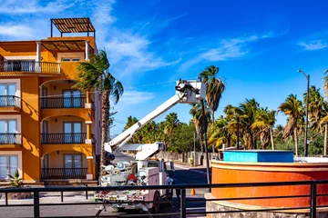 Fototapete Palme Hydraulic truck with bucket lift parked on street next to building. Telescopic boom lift and bucket platform are elevated toward power lines on a pole. Urban power line maintenance in Mexico  © Emile