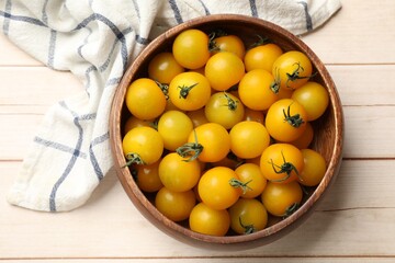 Many fresh yellow tomatoes in bowl on light wooden table, top view