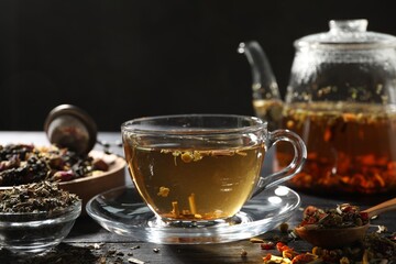 Refreshing herbal tea and dry leaves on black wooden table, closeup. Space for text