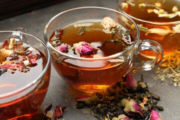 Aromatic herbal tea in glass cups, dry leaves and flowers on grey table, closeup