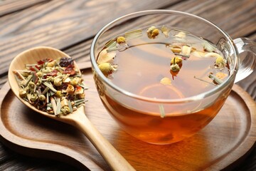 Aromatic herbal tea in glass cup and dry leaves on wooden table, closeup