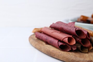 Tasty fruit leather rolls on white tiled table, closeup. Space for text