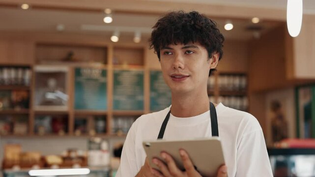 Portrait of cheerful male waiter taking order with tablet in cafe. Handsome man uses digital menu on device working with customers in restaurant. Student cafeteria part-time employee