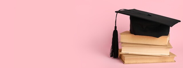 Mortar board and stack of books on pink background with space for text