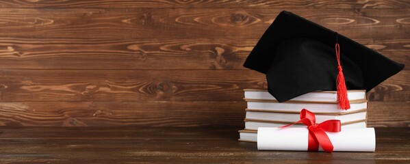 Mortar board, stack of books and diploma on wooden background with space for text
