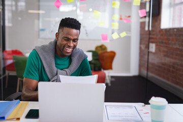 African American man reviewing documents at coworking desk, with laptop binders and sticky notes