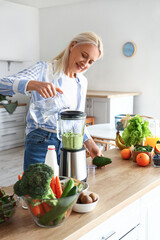 Mature woman making healthy smoothie with blender in kitchen