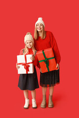 Cute little girl and her mother with Christmas gift boxes on red background