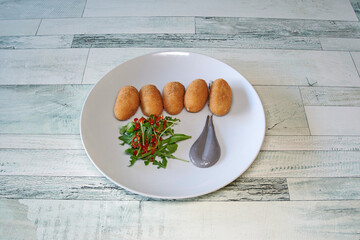 A plate of food with a spoon on it. The spoon is grey and has a greyish-blue color. The plate has a few pieces of food on it, including a few pieces of food that look like donuts
