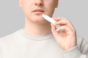 Young man with lip balm on grey background, closeup