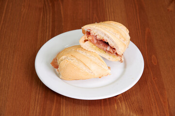 A sandwich is cut in half and placed on a white plate. The sandwich is on a wooden table