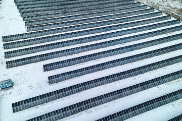 Aerial view of snow covered sustainable electric power plant with rows of solar photovoltaic panels...