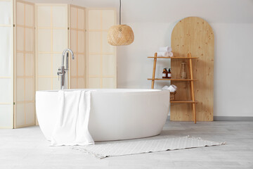 Bathtub with towel, shelving unit and folding screen in interior of bathroom